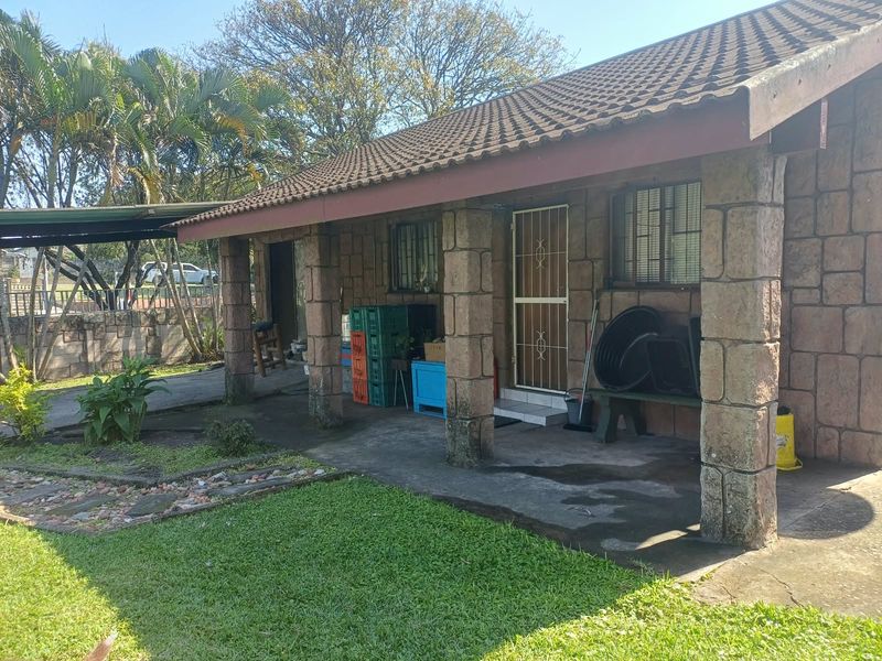 A covered patio area featuring stone-clad columns and a tiled roof, overlooking a garden space.