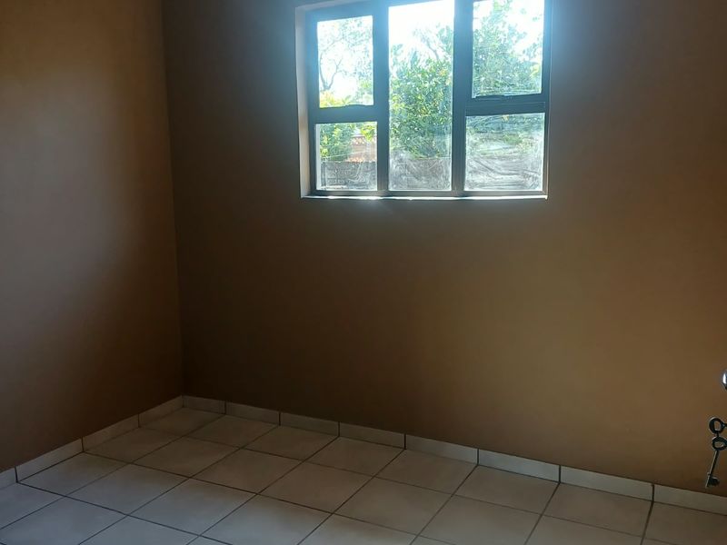 A vacant bedroom featuring neutral wall paint, white ceramic floor tiles, and an aluminium-framed window providing natural light.