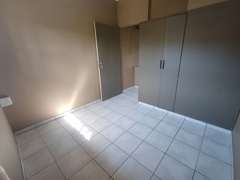 A clean, empty bedroom featuring neutral wall tones, tiled flooring, and built-in cupboards, offering a versatile space ready for personalization.