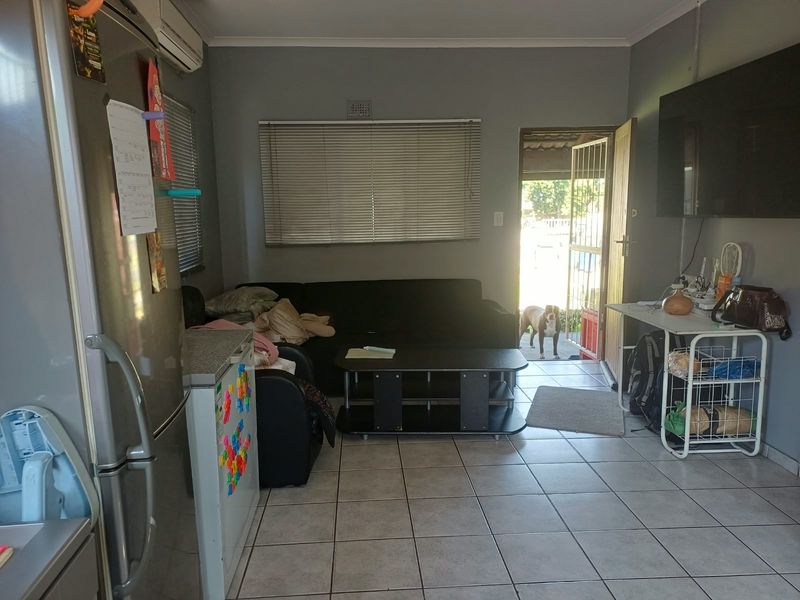 A functional living area featuring tiled flooring, a wall-mounted air conditioning unit, and natural light entering through the doorway.