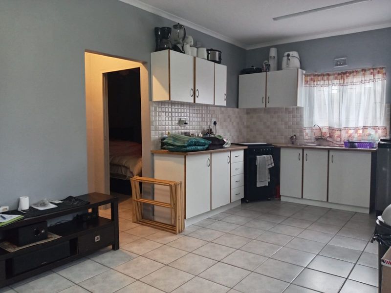 A functional kitchen featuring white built-in cabinetry, tiled backsplash, and ceramic floor tiles, offering a practical layout with direct access to adjacent rooms.