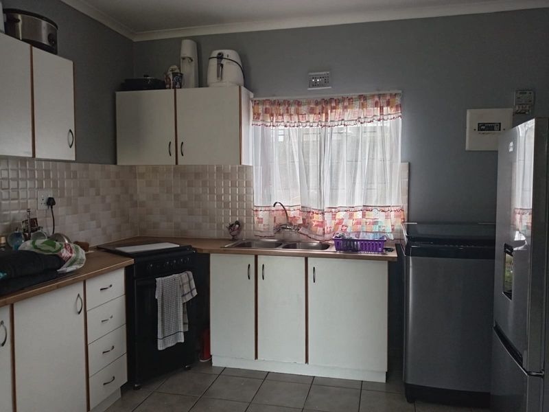 A functional kitchen featuring white cabinetry, laminate countertops, a double sink, and tiled backsplash, offering a practical layout for daily meal preparation.