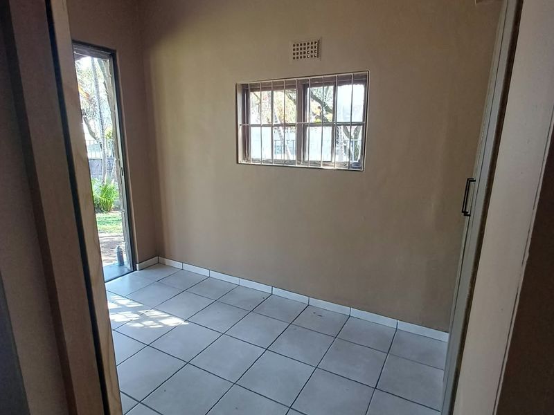 An empty bedroom featuring tiled flooring, a window with security bars, and direct access to the exterior garden area.
