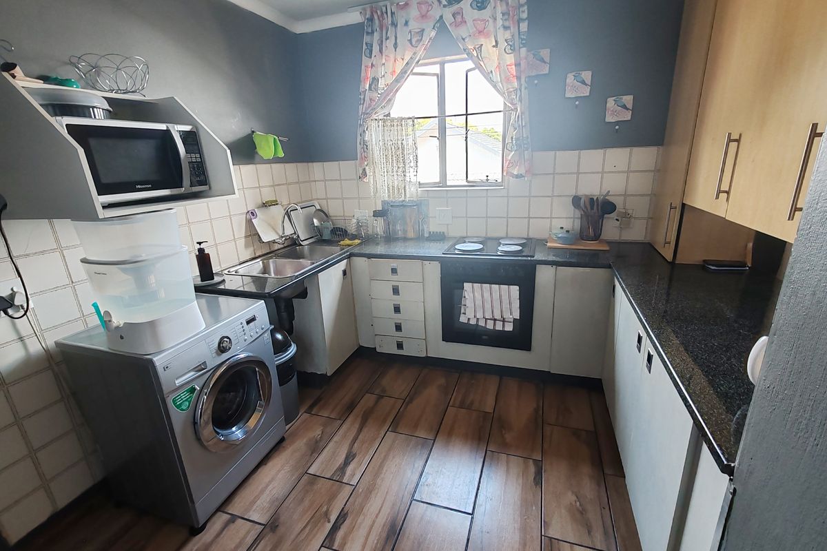 Compact kitchen featuring built-in cabinetry, granite countertops, integrated oven and hob, and wood-look floor tiles.