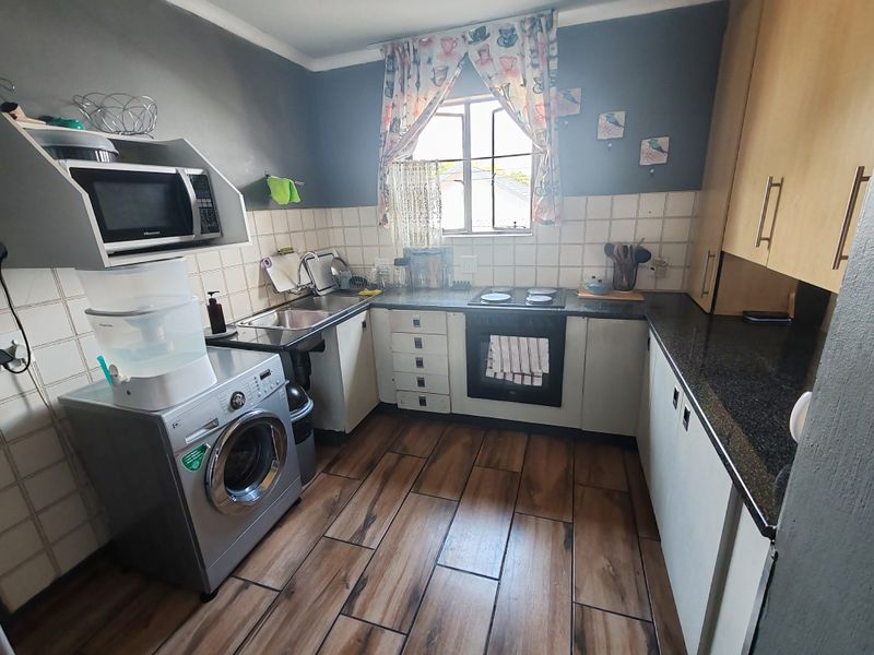 Compact kitchen featuring built-in cabinetry, granite countertops, integrated oven and hob, and wood-look floor tiles.