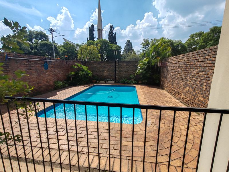 A private outdoor pool area featuring a swimming pool surrounded by brick paving and enclosed by high brick boundary walls and a metal safety fence.