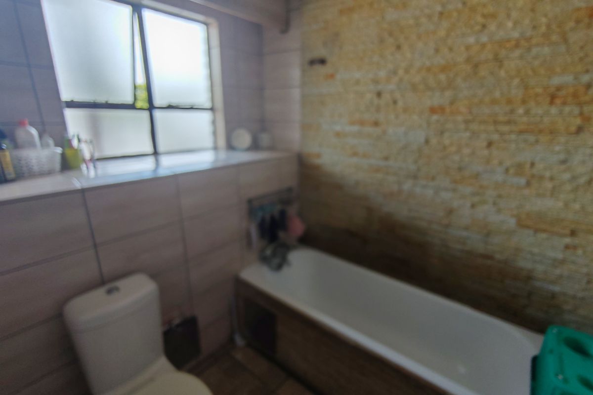 Bathroom featuring a bathtub, toilet, and a decorative stone-clad feature wall with tiled surrounds and a window for natural light.