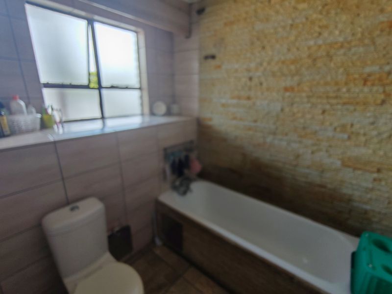 Bathroom featuring a bathtub, toilet, and a decorative stone-clad feature wall with tiled surrounds and a window for natural light.