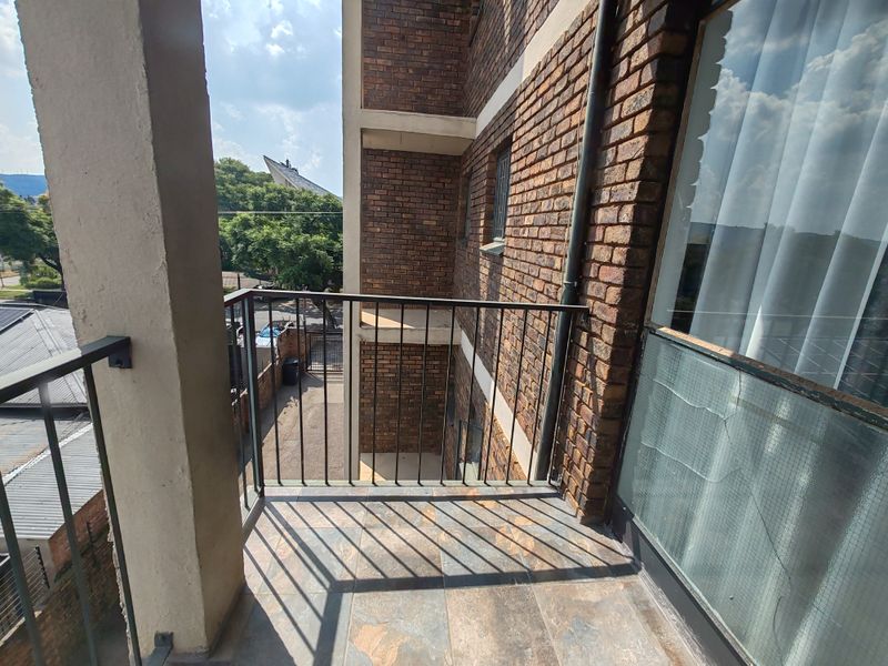 A private balcony featuring tiled flooring, a metal balustrade, and exposed brick exterior walls, offering an outdoor space with a view of the building surroundings.