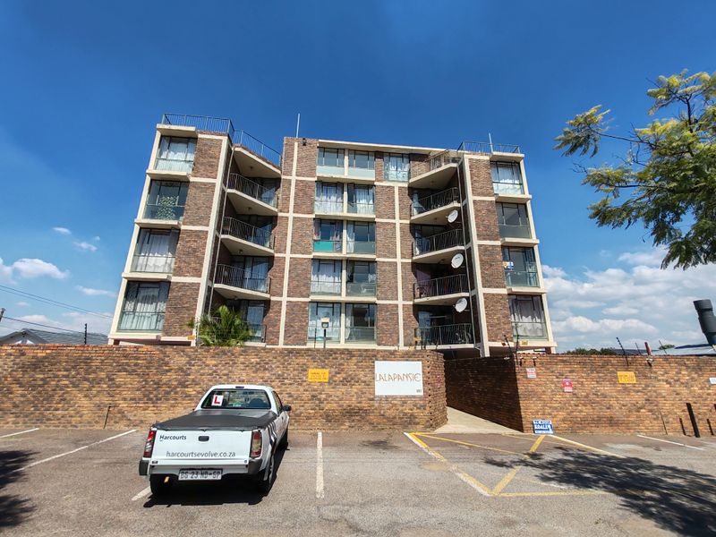 Front elevation of the Lalapansie apartment complex featuring a multi-story brick facade with private balconies and an associated paved parking area.