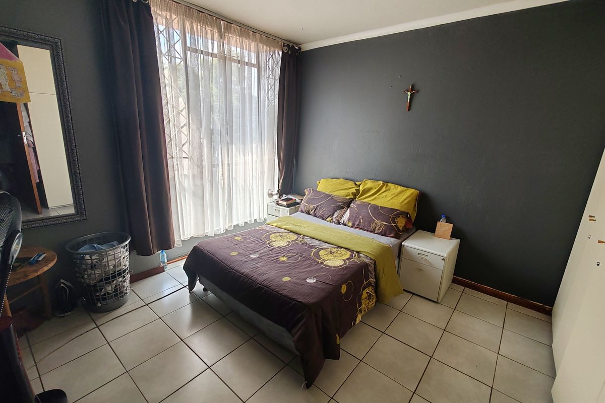 A bedroom featuring tiled flooring, a large window with security gate, and built-in storage space.