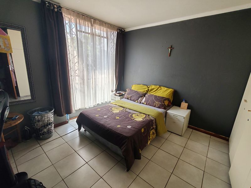 A bedroom featuring tiled flooring, a large window with security gate, and built-in storage space.