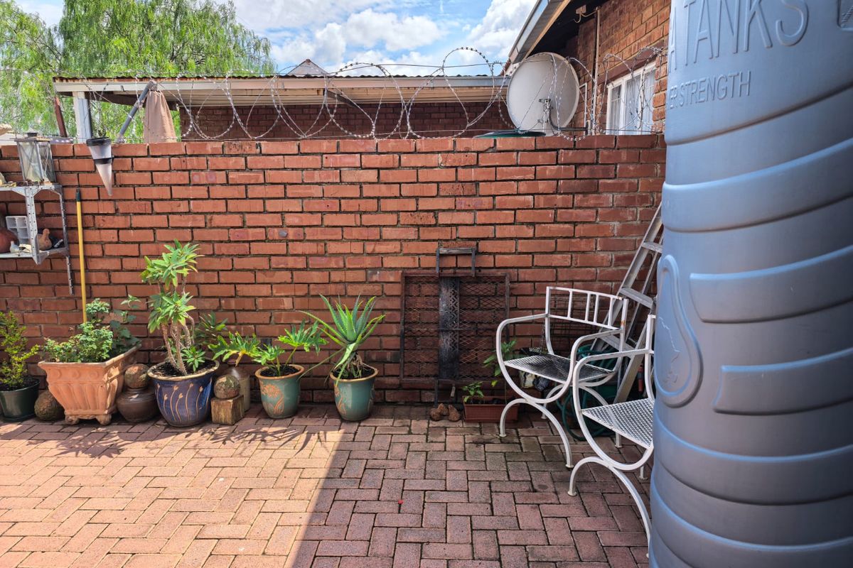 A private rear courtyard featuring brick boundary walls with security razor wire, paved flooring, and a large integrated water storage tank.