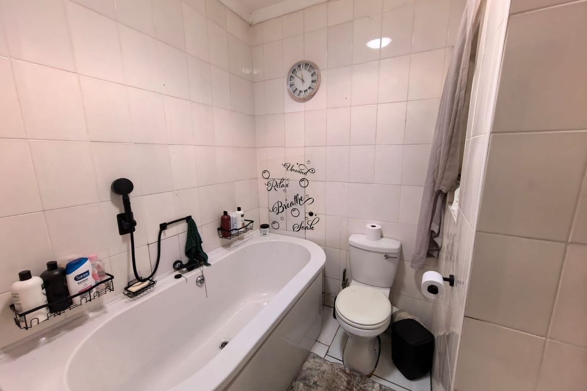 A compact bathroom featuring a standard bathtub, toilet, and full-height wall tiling. The space would benefit from modern updates to finishes and fixtures.