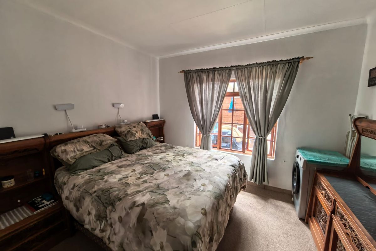 A functional bedroom featuring carpeted flooring, wall-mounted reading lights, and a timber-framed window allowing natural light.