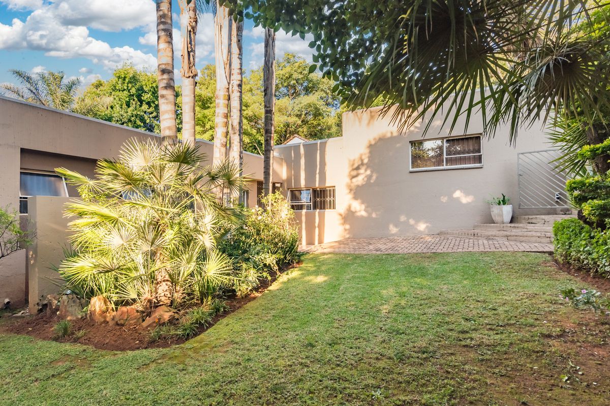 A rear view of the property featuring a paved patio area, established garden with mature trees, and exterior building facade with security window bars.