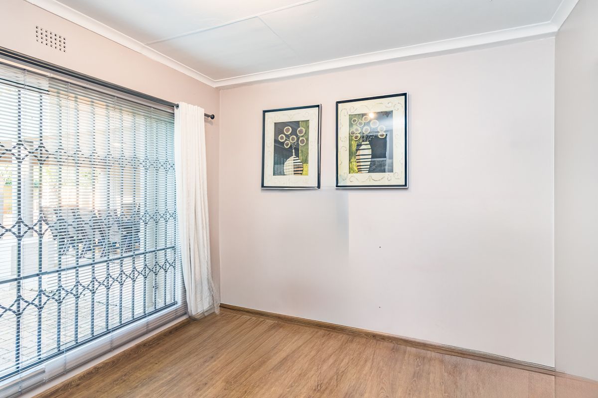 A bright, empty bedroom featuring laminate flooring, a sliding glass door with a security gate, and neutral wall finishes.