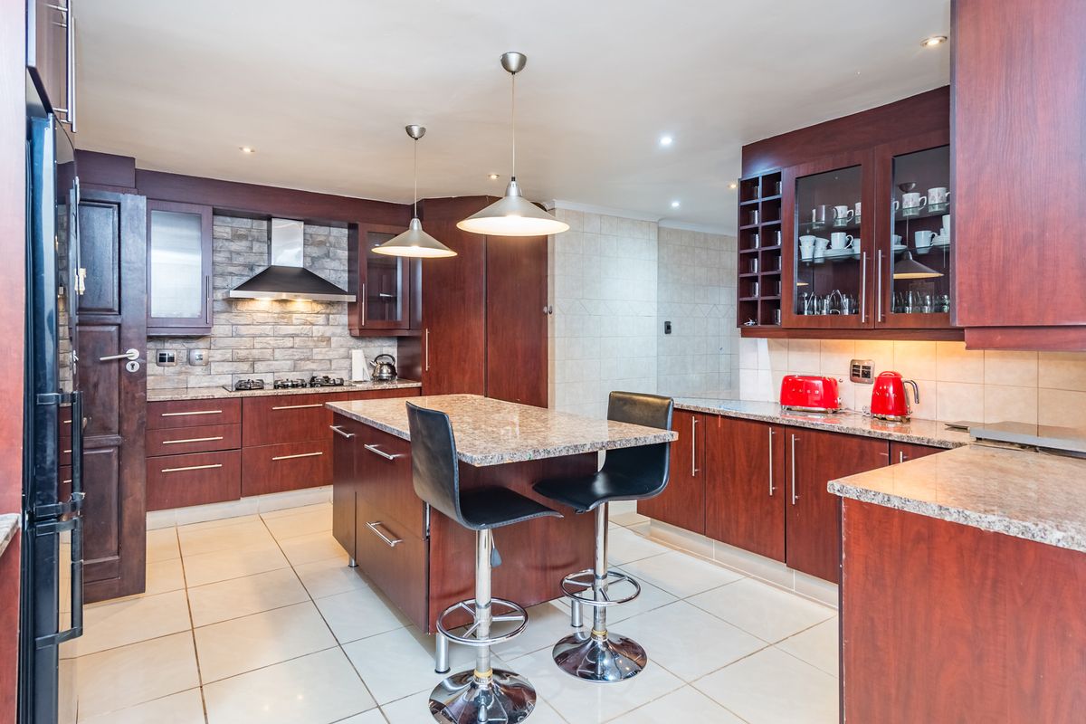 A spacious kitchen featuring dark wood cabinetry, granite countertops, a central island with seating, and a stone veneer backsplash with a gas hob.