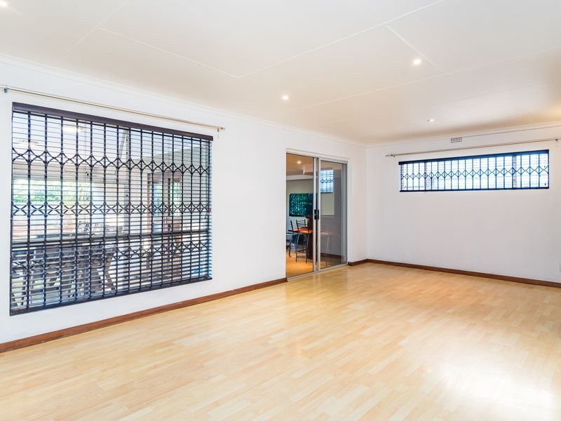 A bright, empty living room featuring laminate flooring, recessed downlights, and sliding glass doors with security gates.