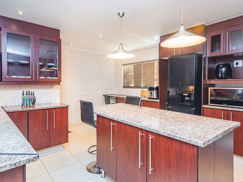 A well-appointed kitchen featuring dark wood cabinetry, granite countertops, a central island, and modern pendant lighting, offering a functional and stylish cooking space.