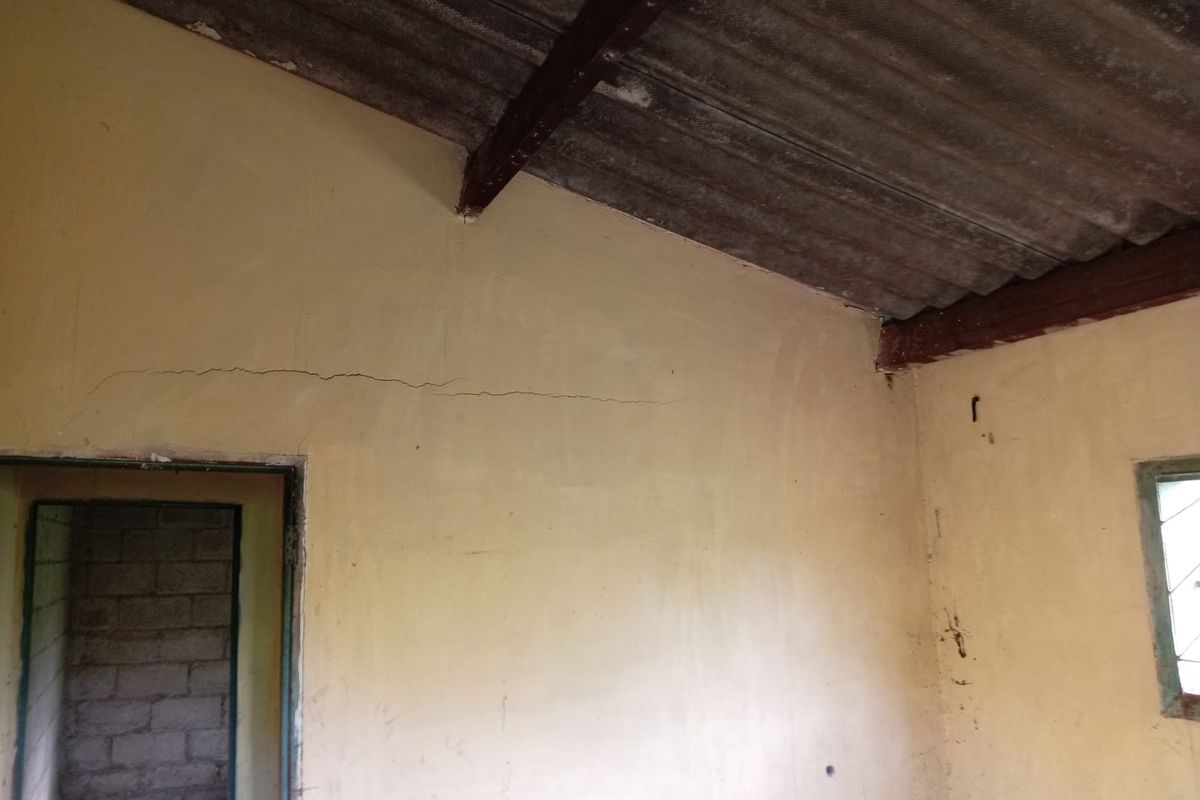 An empty room featuring exposed timber rafters, corrugated roofing, and a steel-framed window, requiring significant renovation and repair to the wall surfaces.