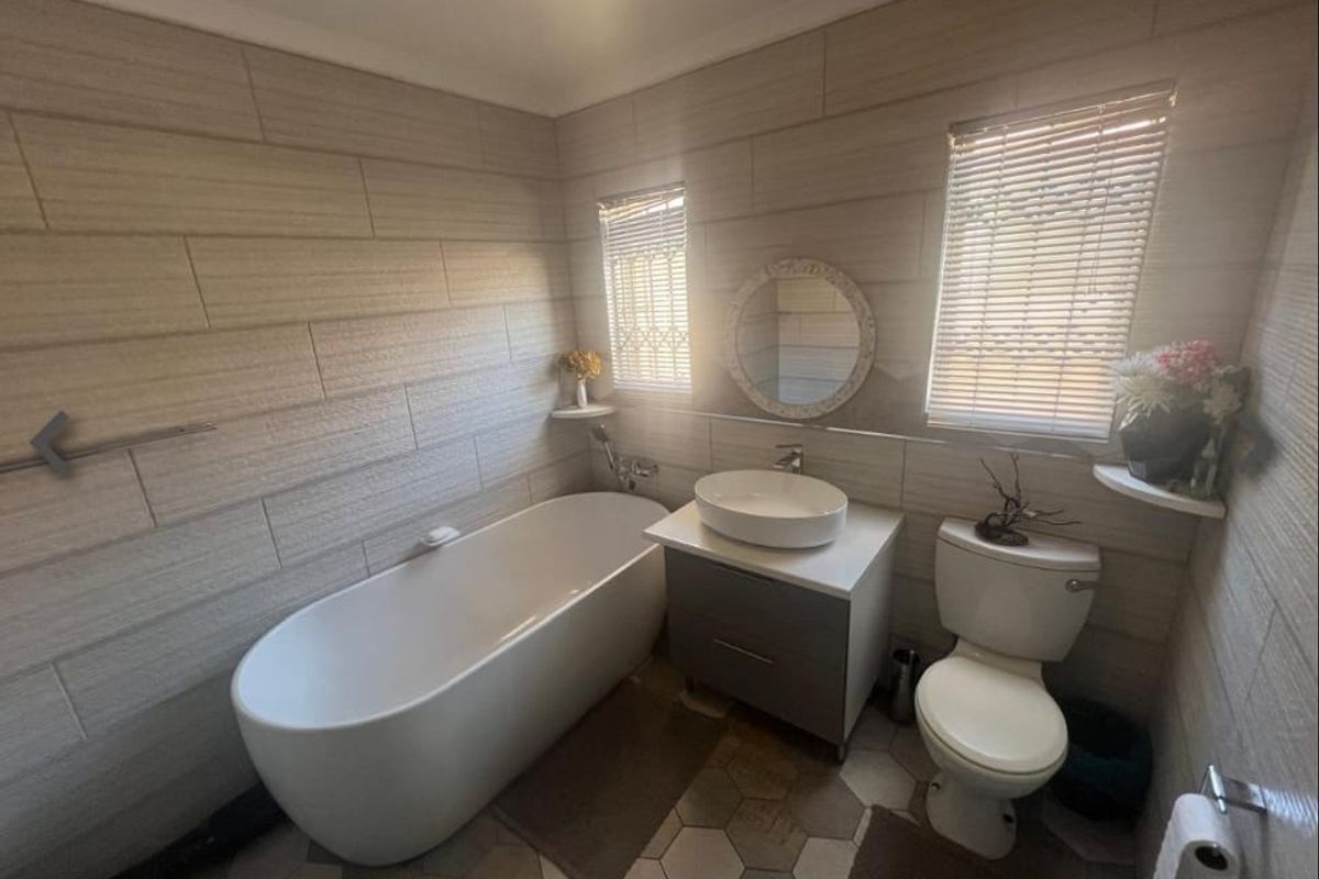 Modern bathroom featuring a freestanding bathtub, vessel sink on a vanity cabinet, toilet, and stylish hexagonal floor tiles with neutral wall tiling.