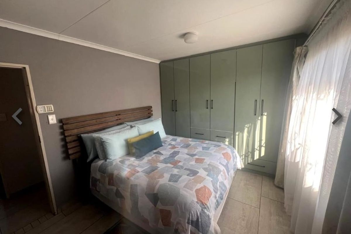 A well-maintained bedroom featuring neutral wall tones, tiled flooring, and extensive floor-to-ceiling built-in cupboards for ample storage.