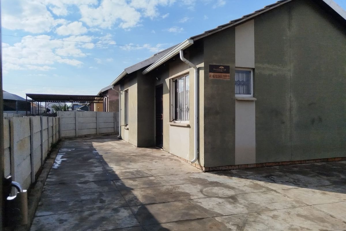 Side view of a townhouse featuring a paved courtyard area, perimeter boundary wall, and tiled roof structure.