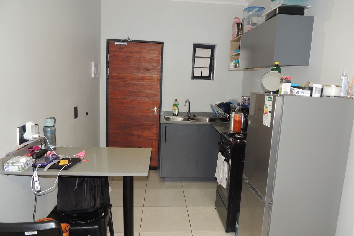 Compact kitchen featuring grey cabinetry, tiled flooring, a stainless steel sink, and a freestanding stove, providing a functional cooking and preparation space.