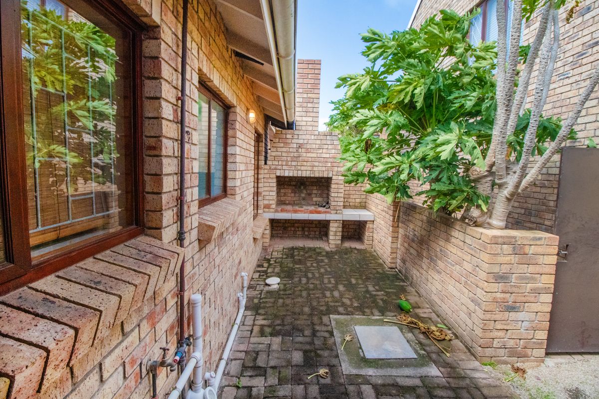 A private outdoor courtyard featuring a built-in brick braai area, paved flooring, and perimeter brick walls.