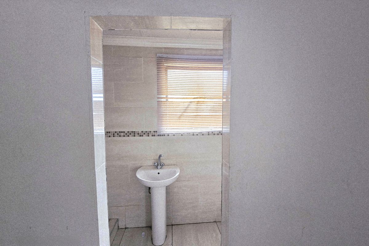 A compact bathroom featuring a pedestal basin, neutral wall and floor tiling, and a window with a fitted venetian blind.