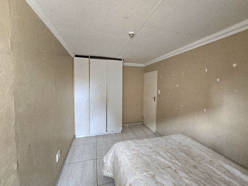 A bedroom featuring tiled flooring, a built-in wardrobe, and coved ceilings, currently requiring wall repairs and cosmetic updates.
