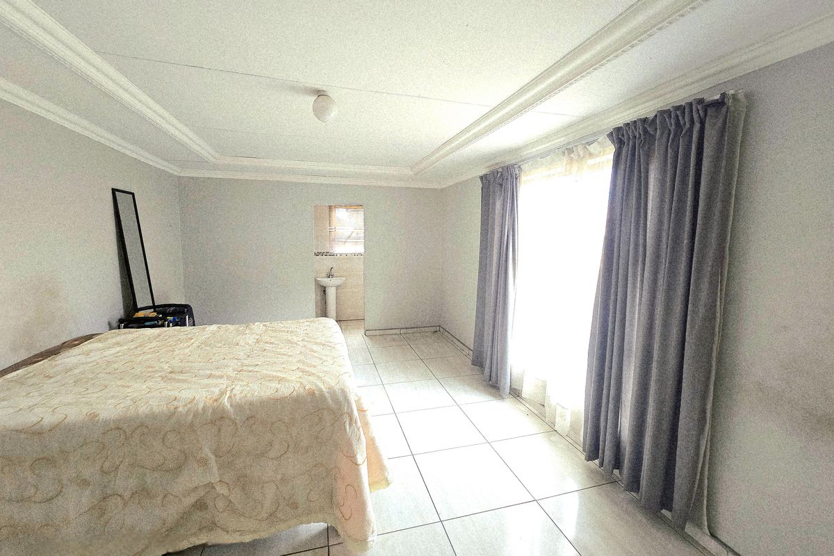 Spacious bedroom featuring tiled flooring, decorative ceiling cornicing, and an integrated en-suite pedestal basin area.