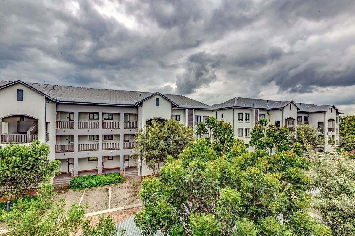 Exterior view of a multi-story apartment complex featuring paved parking areas, landscaped greenery, and covered balcony walkways.
