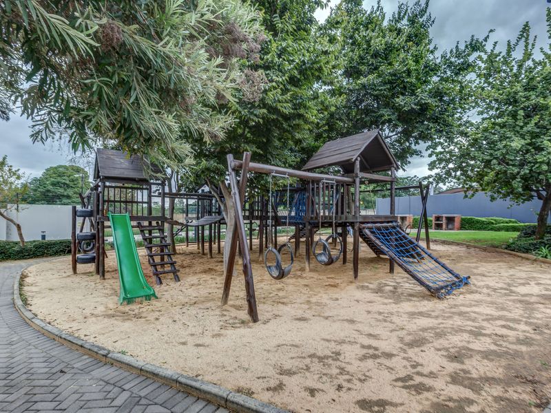 Communal outdoor play area featuring a wooden jungle gym, swings, slide, and climbing net set within a sand pit.