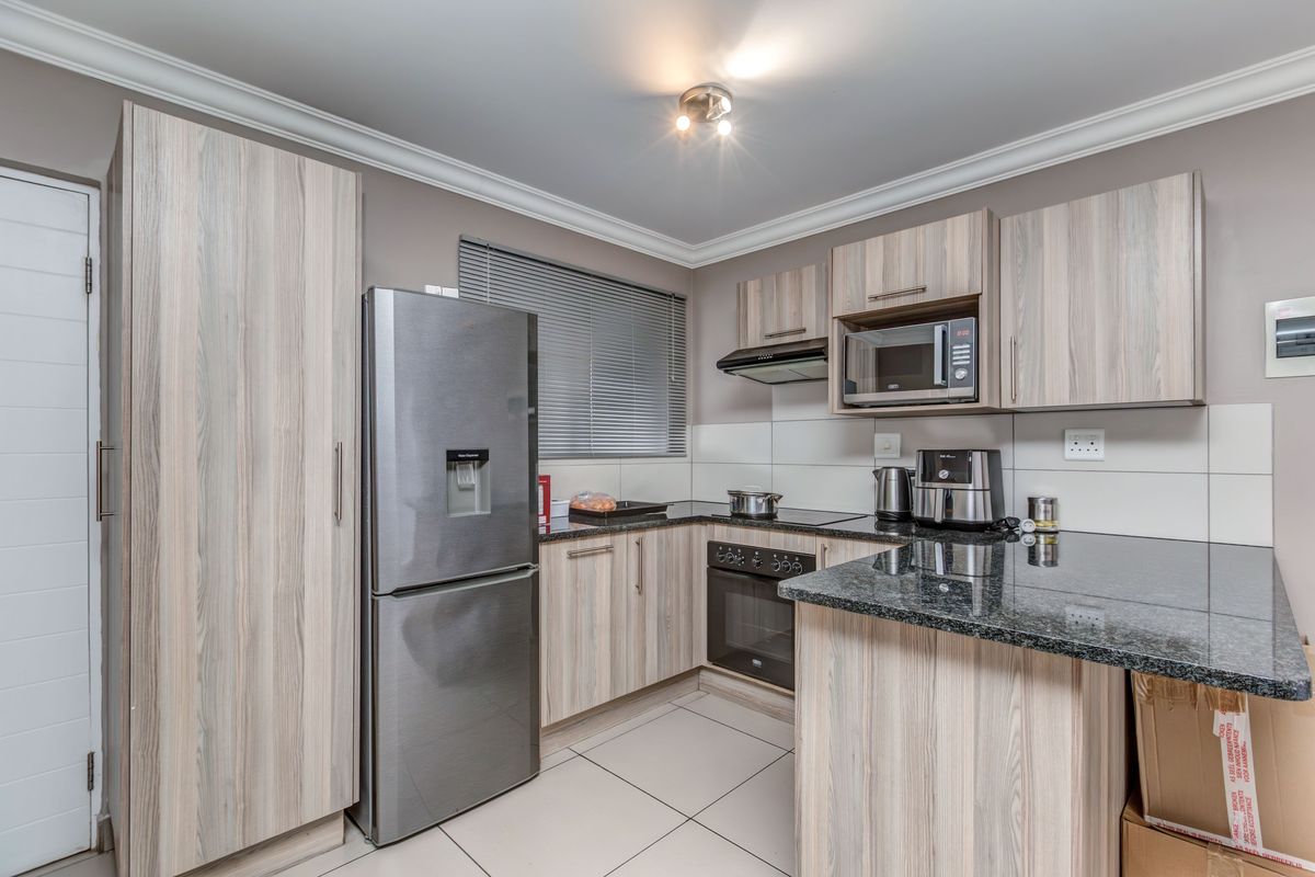 Modern kitchen featuring light wood-grain cabinetry, granite countertops, built-in oven, extractor fan, and tiled flooring.