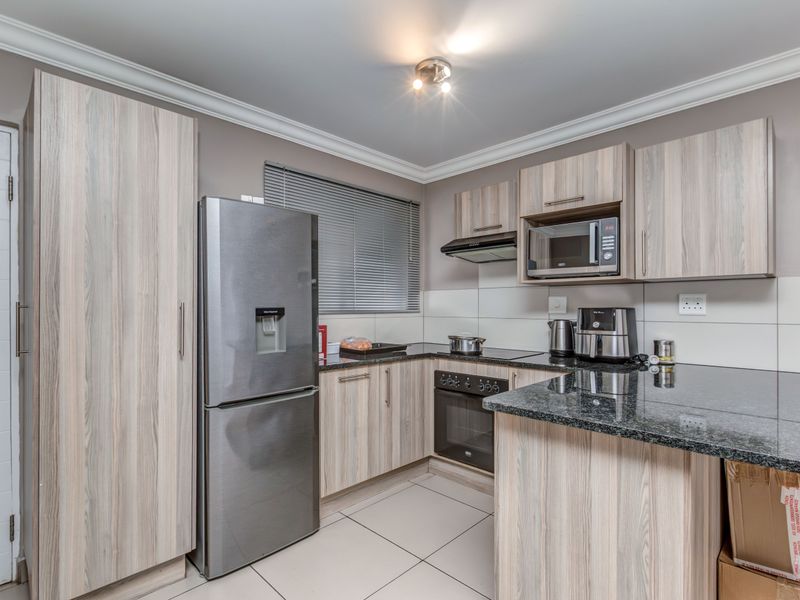 Modern kitchen featuring light wood-grain cabinetry, granite countertops, built-in oven, extractor fan, and tiled flooring.