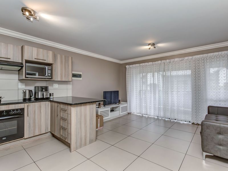 Open-plan living area featuring a modern kitchen with built-in oven, hob, extractor fan, and tiled flooring throughout, leading to a bright balcony space.