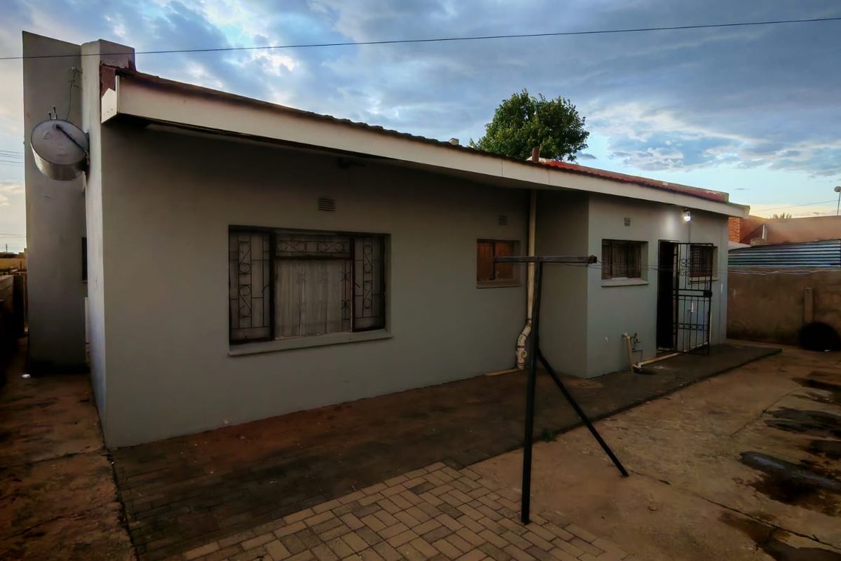 Rear exterior view of the house featuring a paved patio area, security gates, and a wall-mounted geyser.