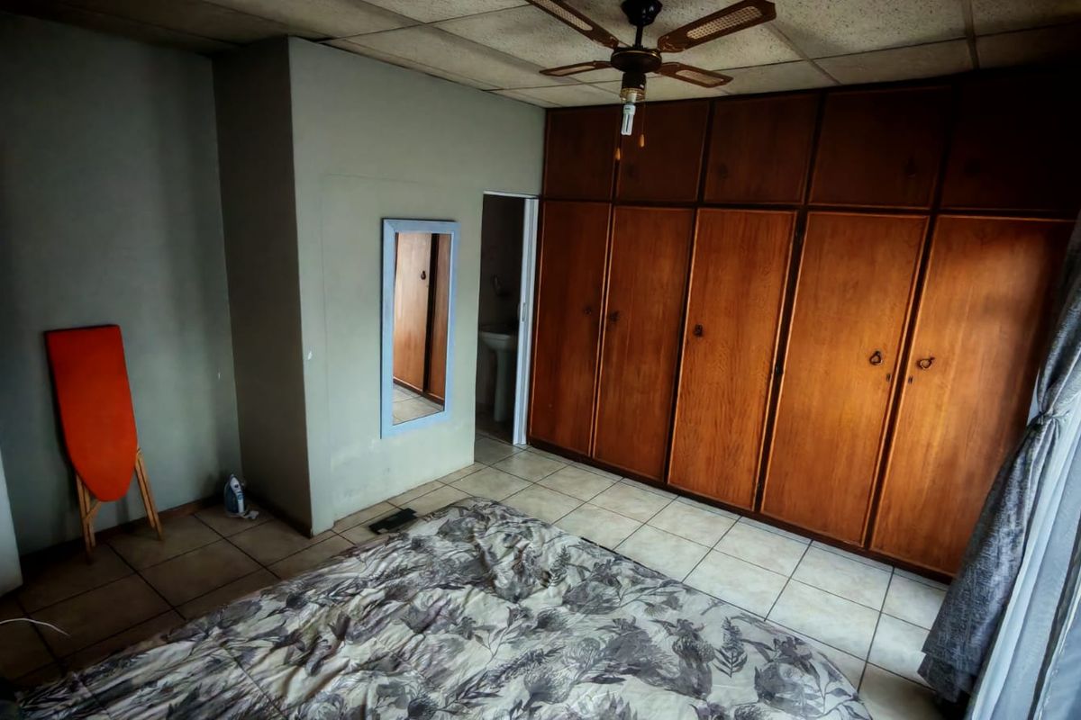 A bedroom featuring built-in wooden cabinetry, tiled flooring, and a ceiling fan, offering a functional space with potential for cosmetic updates.