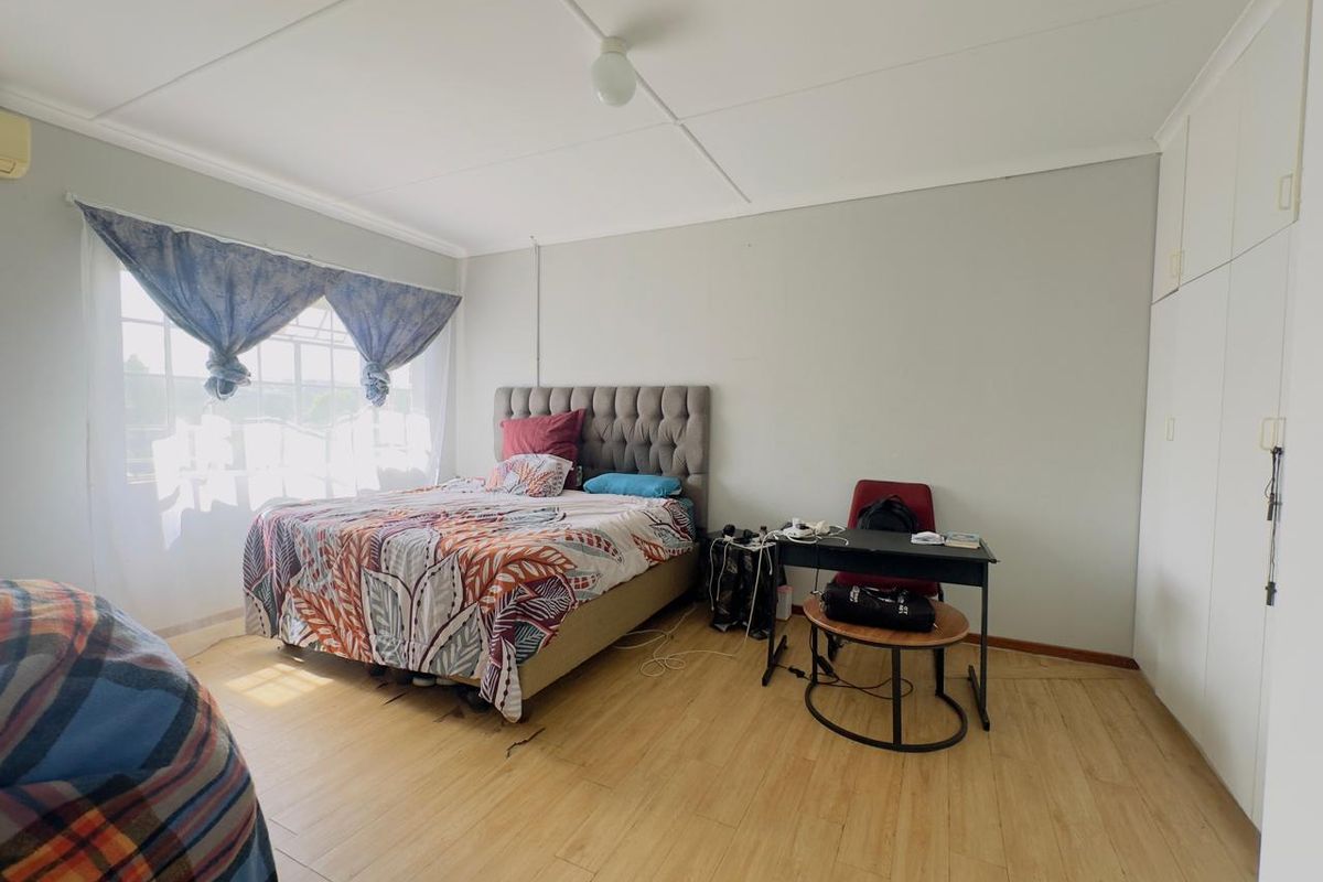 A spacious bedroom featuring light wood-look flooring, built-in floor-to-ceiling wardrobes, and large windows allowing for ample natural light.