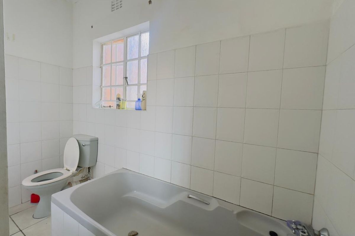 A functional bathroom featuring a standard bathtub, toilet, and white wall tiling throughout.