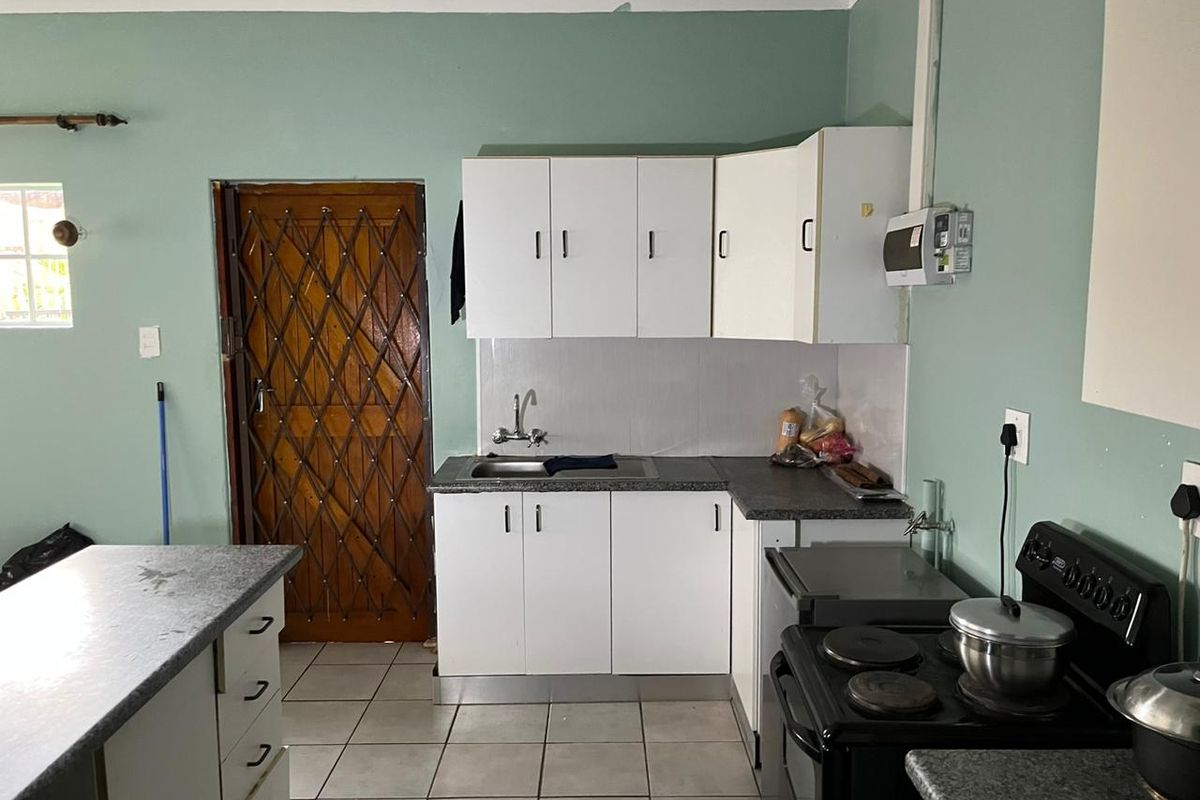A functional kitchen featuring white cabinetry, tiled flooring, a stainless steel sink, and a freestanding electric stove.