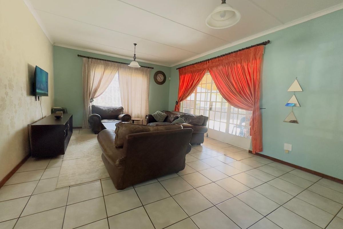 A spacious living room featuring tiled flooring, large glass sliding doors providing natural light, and access to an outdoor patio area.