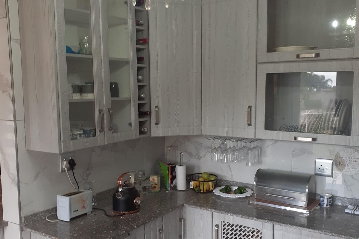 A well-maintained kitchen featuring light wood-grain cabinetry, granite countertops, marble-look wall tiles, and a decorative crystal chandelier.