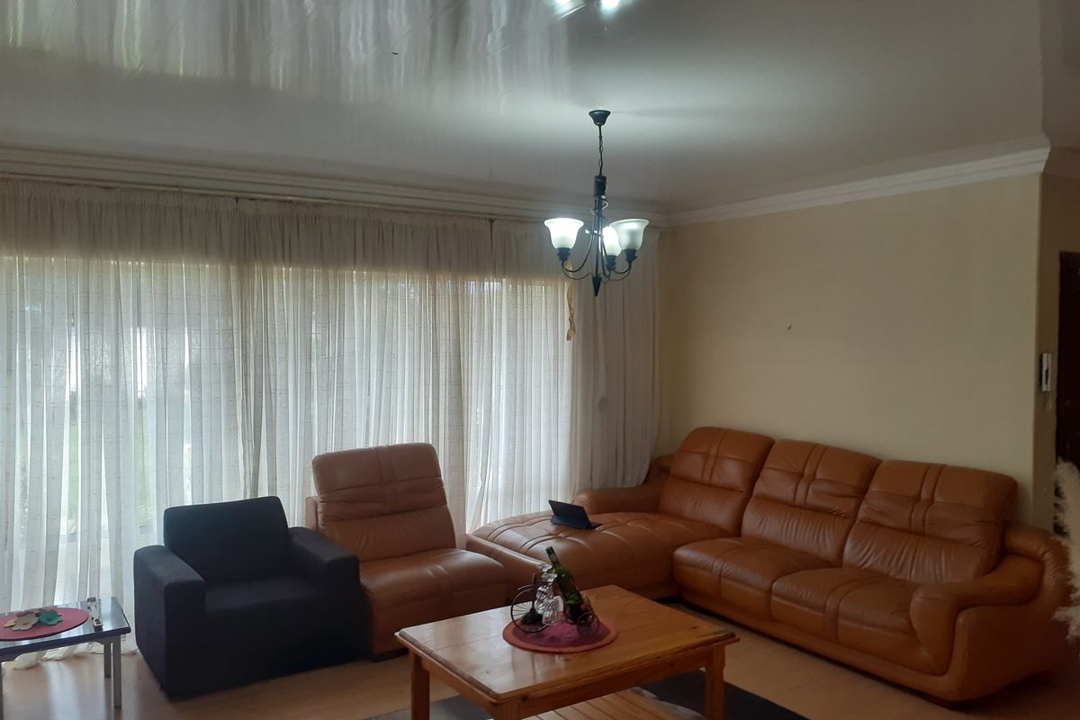 A spacious living room featuring laminate flooring, crown molding, and a large window with floor-to-ceiling curtains, providing ample natural light.