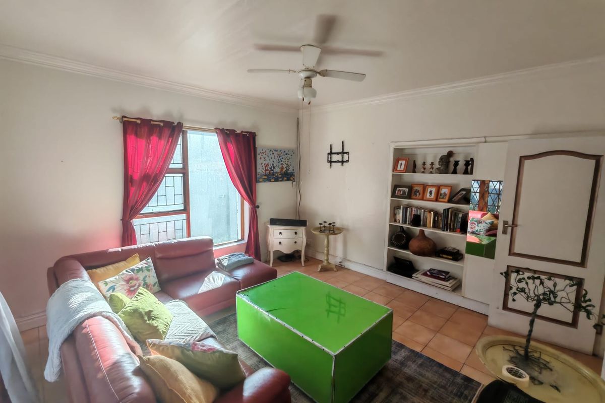 A living room featuring tiled flooring, a ceiling fan, and a built-in shelving unit, offering a functional space with potential for cosmetic updates.