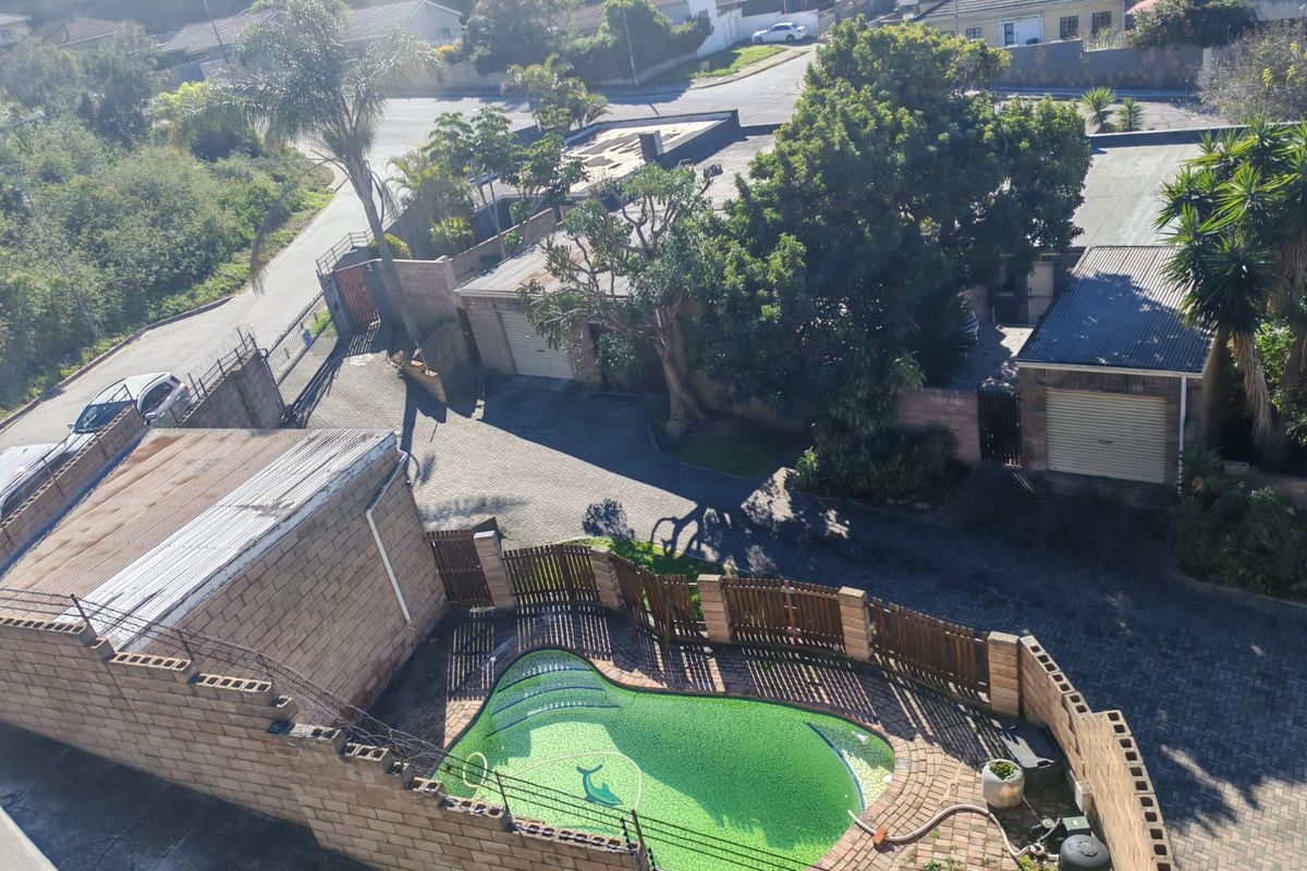 Aerial view of the property showing a swimming pool, paved driveway, garage, and surrounding boundary walls within a residential townhouse complex.