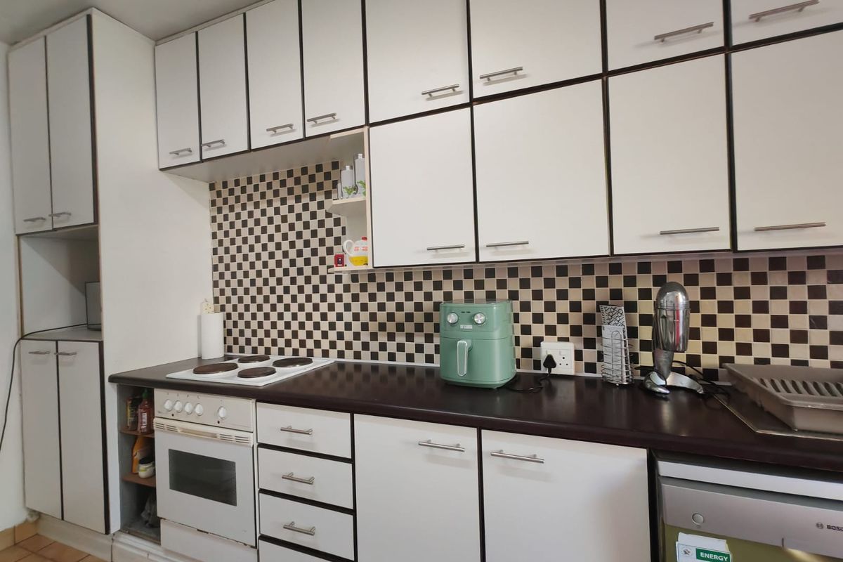 A functional kitchen featuring white cabinetry, dark laminate countertops, a checkered tile backsplash, and built-in cooking appliances.