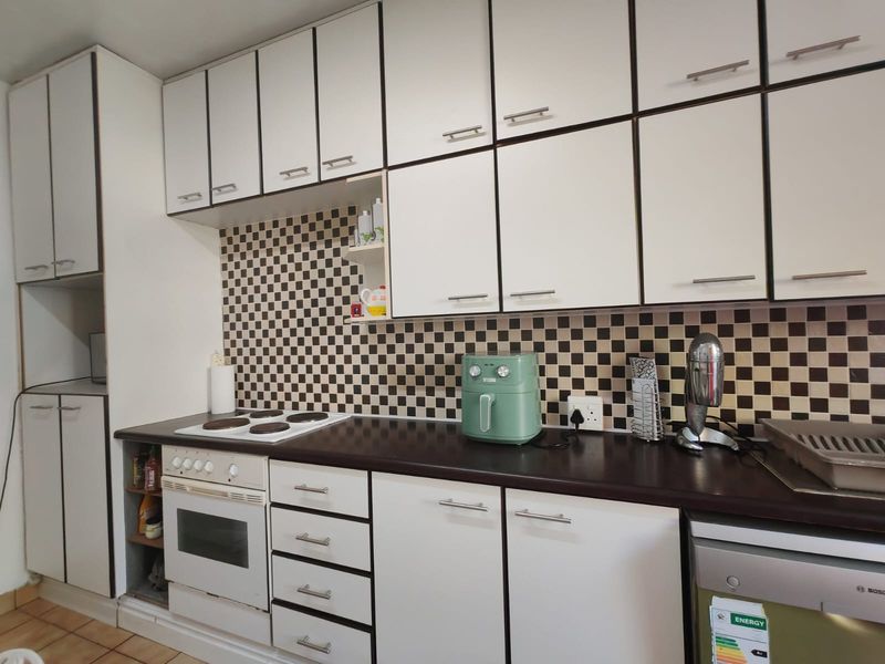 A functional kitchen featuring white cabinetry, dark laminate countertops, a checkered tile backsplash, and built-in cooking appliances.
